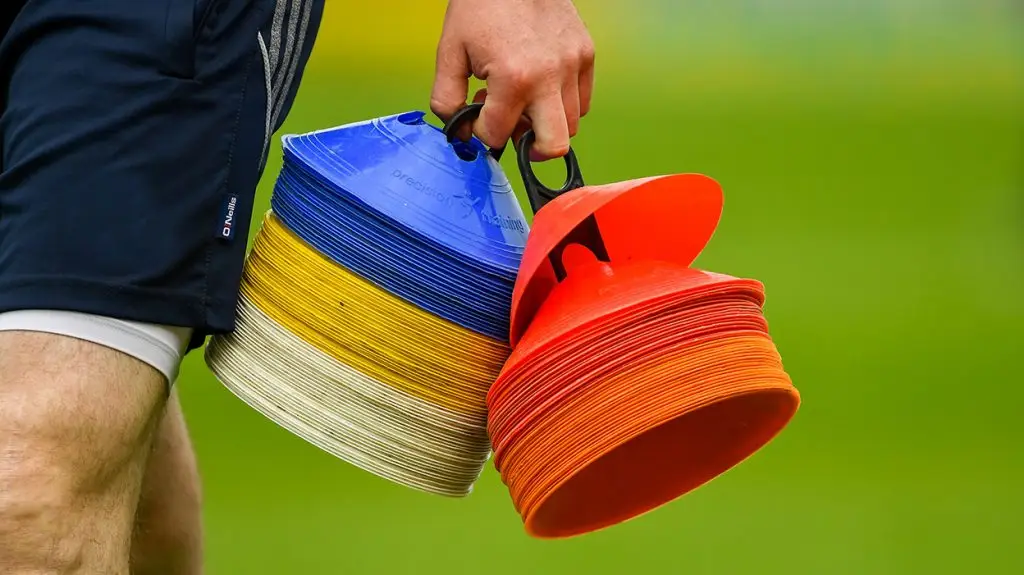Person holding stack of colorful training cones in blue, yellow, white, and red on grass field.