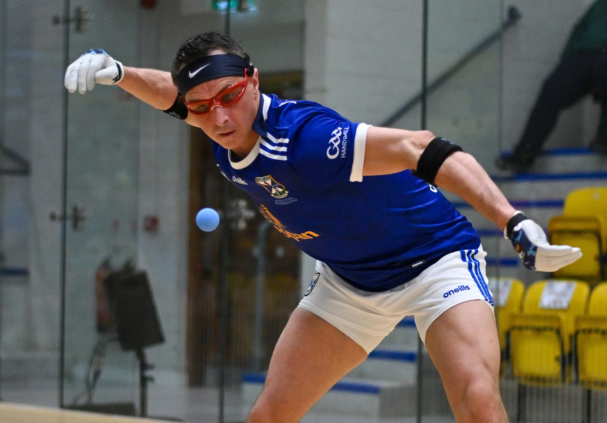 Player in blue and white Laois GAA handball jersey executing a forehand shot on indoor court during match.
